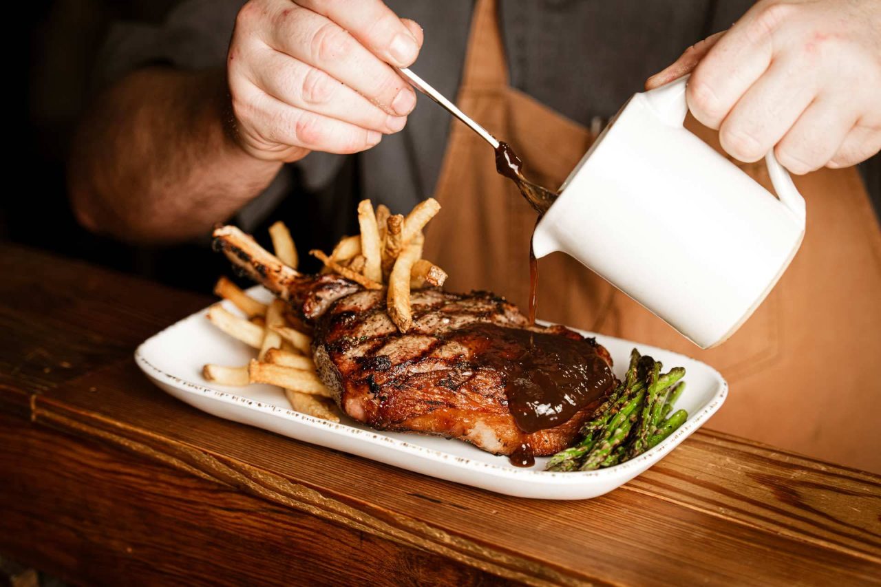 Pan sauce poured over a bone-in ribeye with fries and asparagus