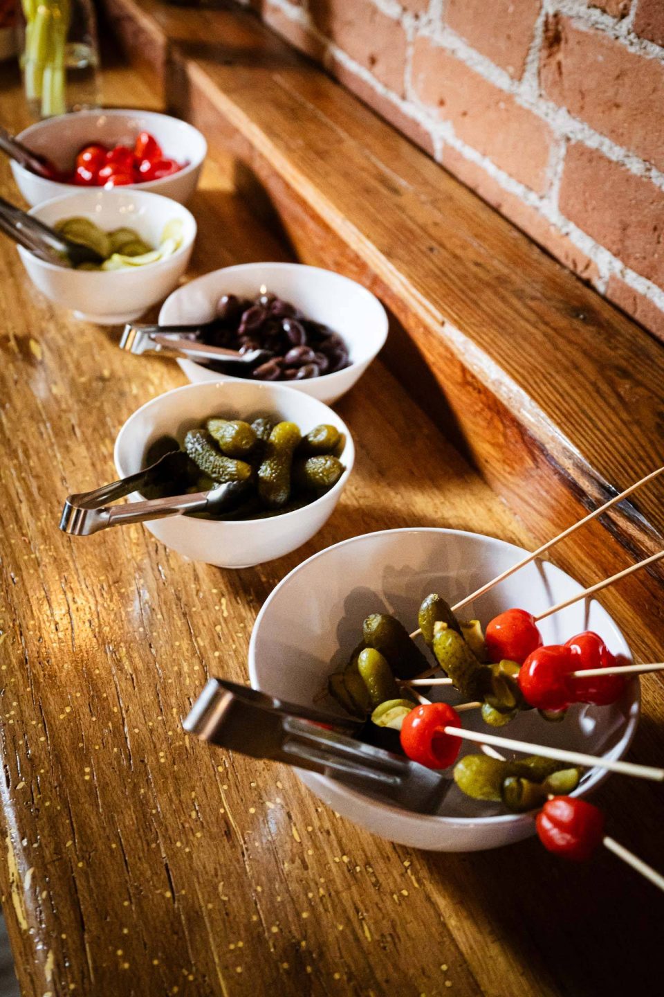 Bloody Mary garnish bar with pickles, olives, and skewers on reclaimed wood